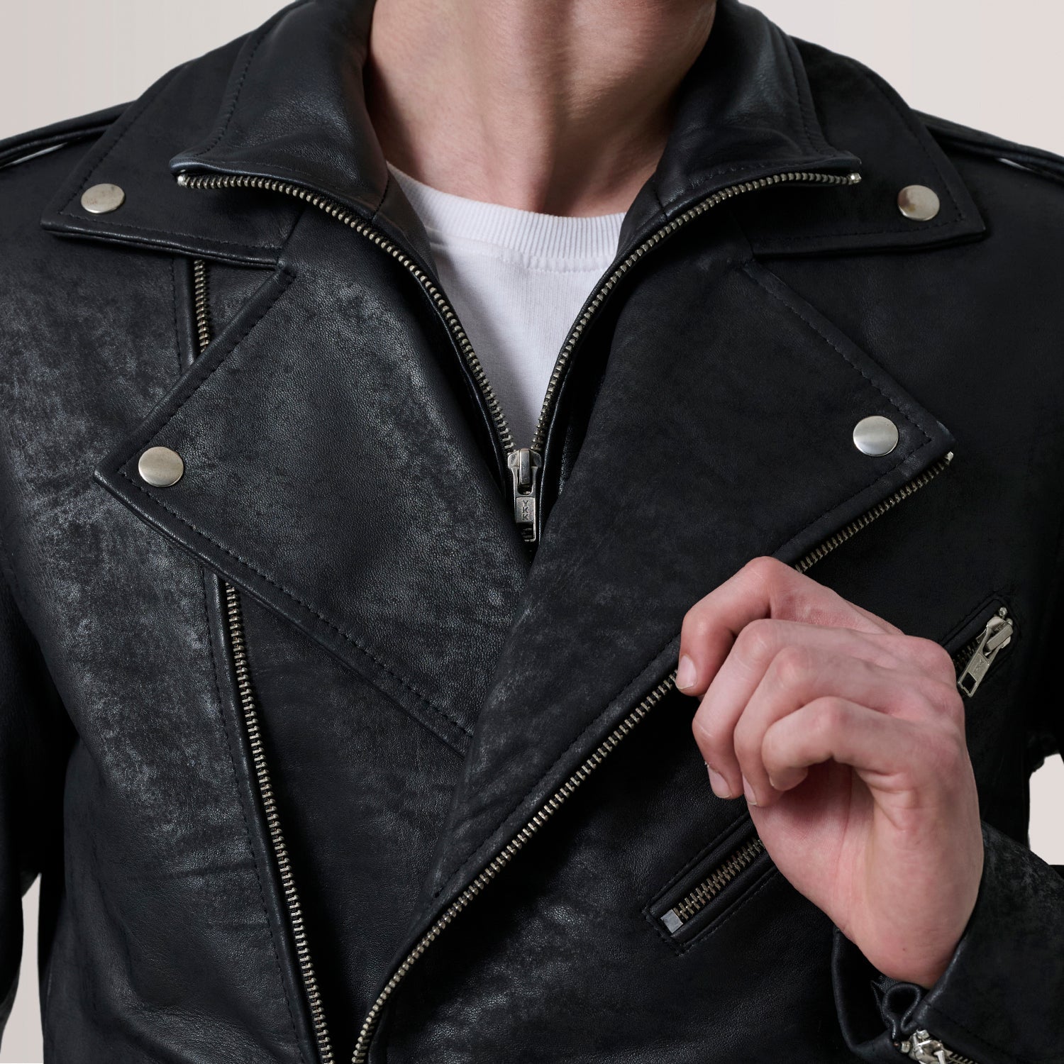 Black leather jacket with silver zippers on a neutral background